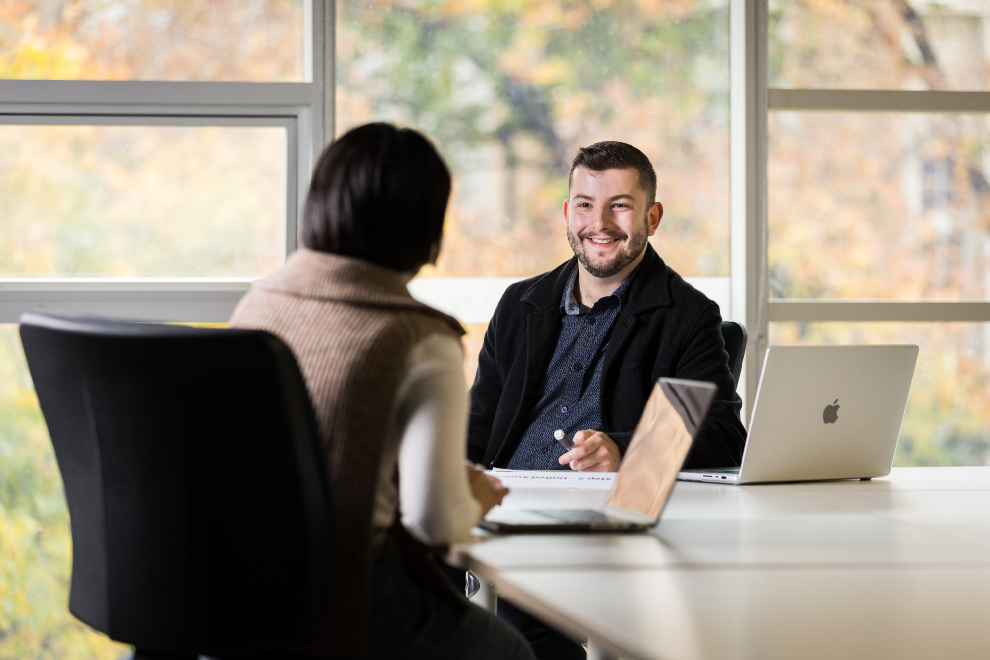 A person smiles at someone sitting across from them at a conference table in front of their laptop
