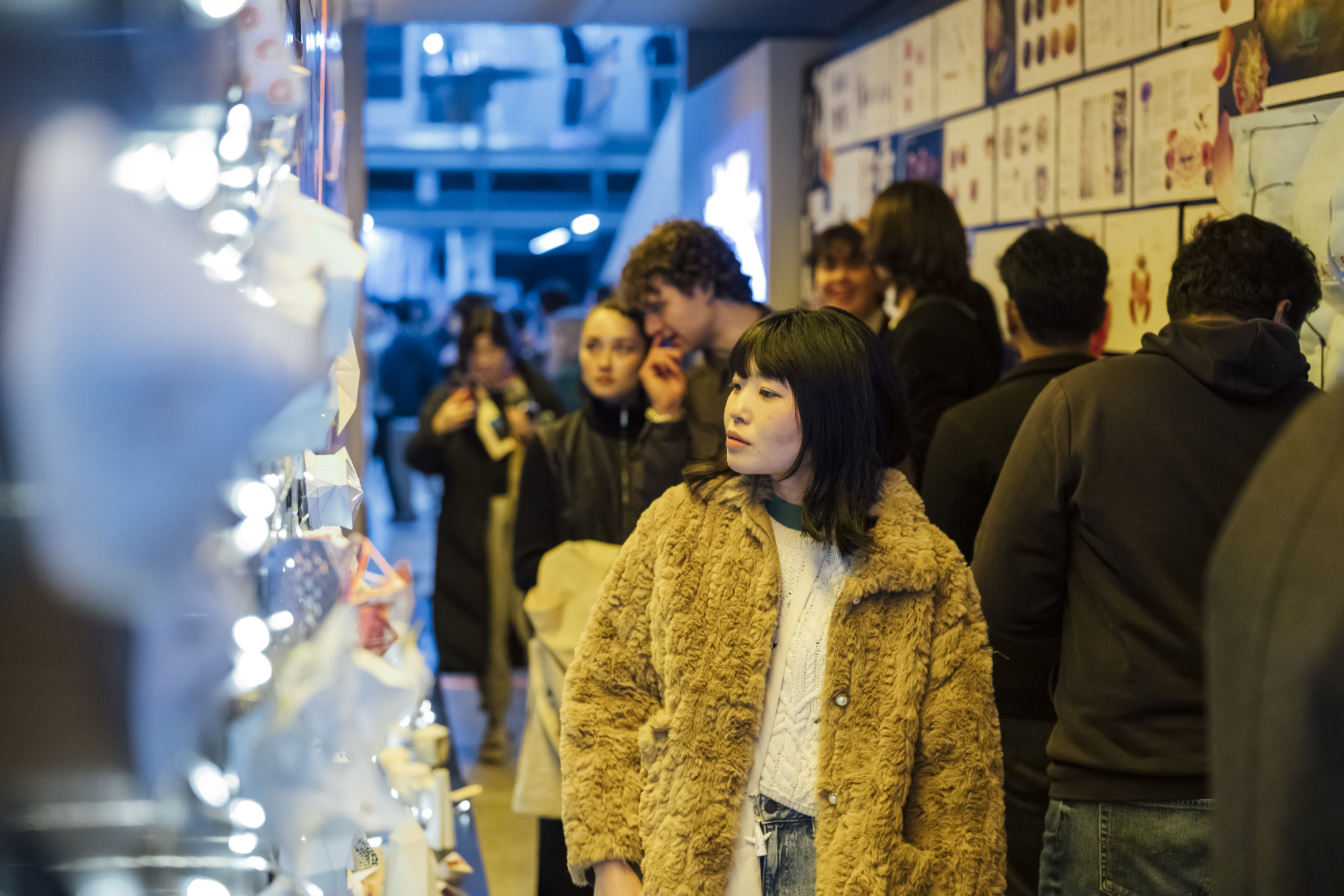 A person in a winter coat stands near fairy lights and a poster display at MSDx