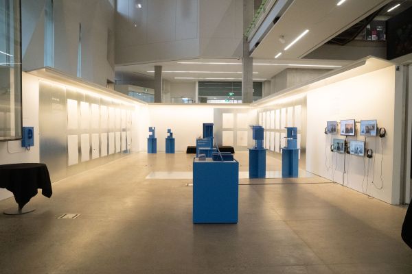 Wide shot image of gallery space. The walls are filled with large sheets of paper and space is filled with a range of blue plinths. 