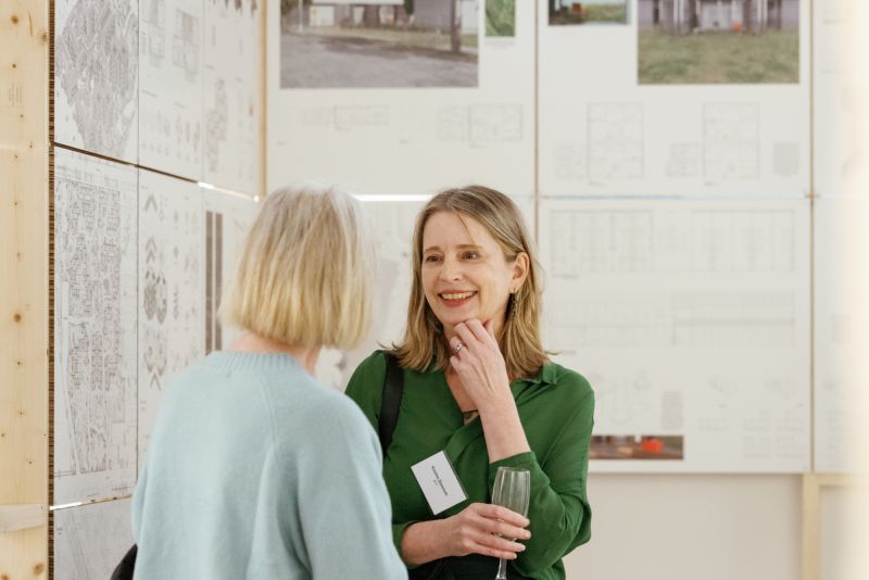two people talking in a gallery, one is holding a wine glass and smiling