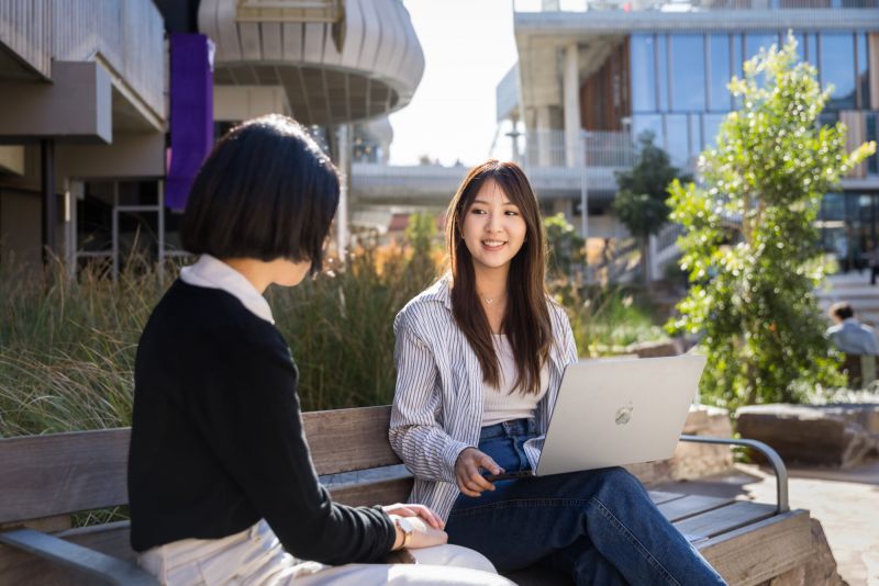 Student with laptop smiling at someone with their back to camera