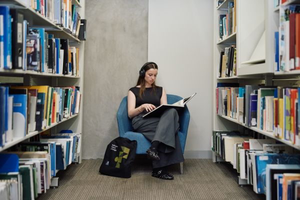 A person sitting in a library with a book wearing headphones