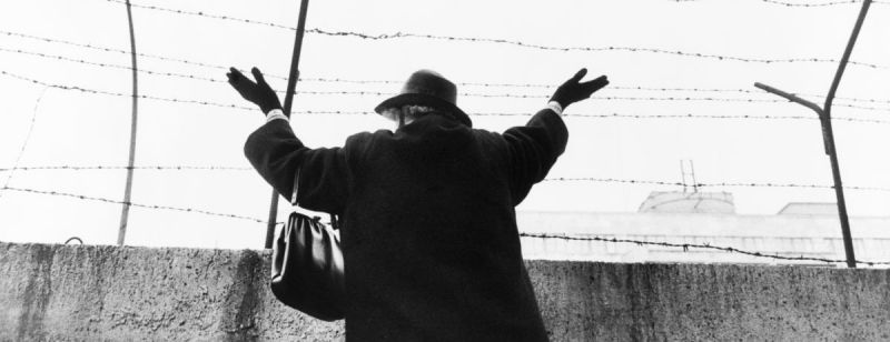 Black and white photo of woman waving over the Berlin Wall