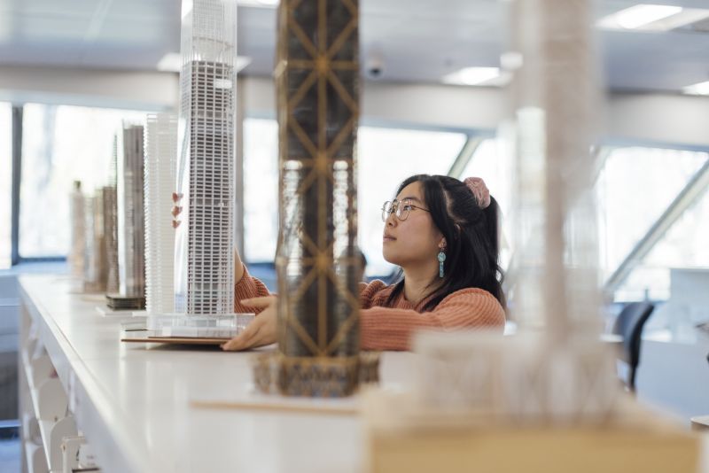 A student places a model on a shelf next to a row of other student models.
