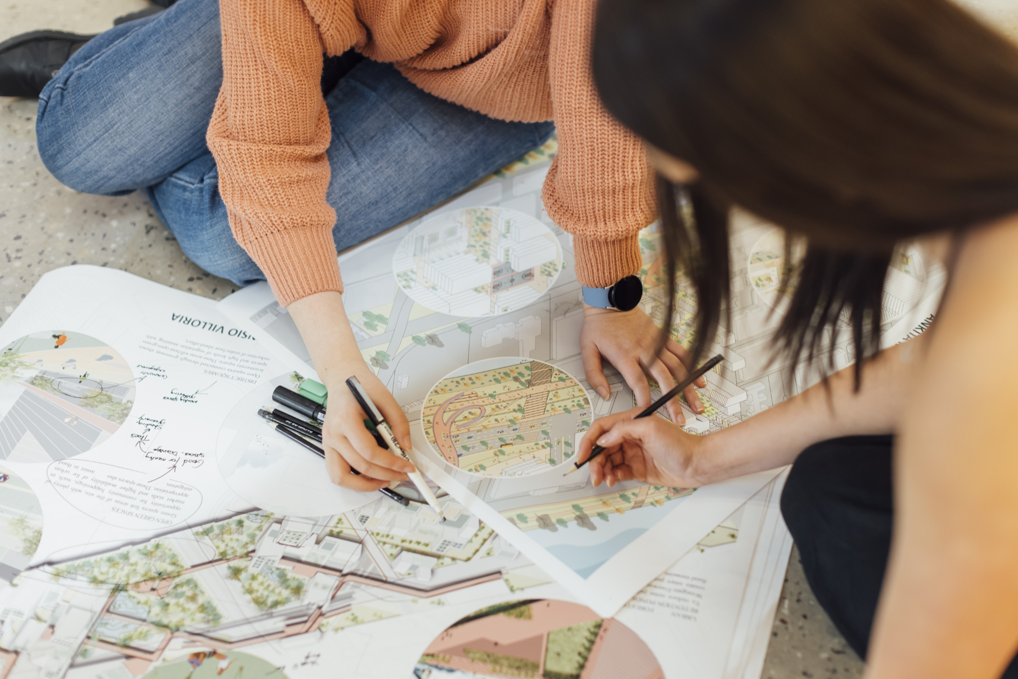 Close up of arms of two students marking up architectural plans