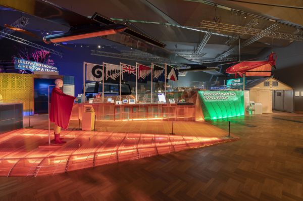 Inside the exhibition - showing a large hall lit up with coloured lights and a row of different, unknown flags