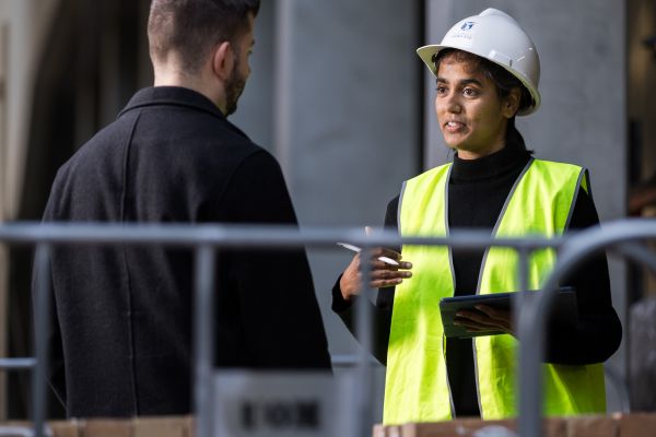 A student in a hardhat in conversation with a professional.