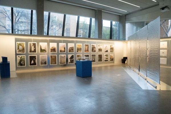 Image shows gallery wall filled with large posters. The space is split diagonally with a silver partition and in the middle of the space is a blue plinth. 