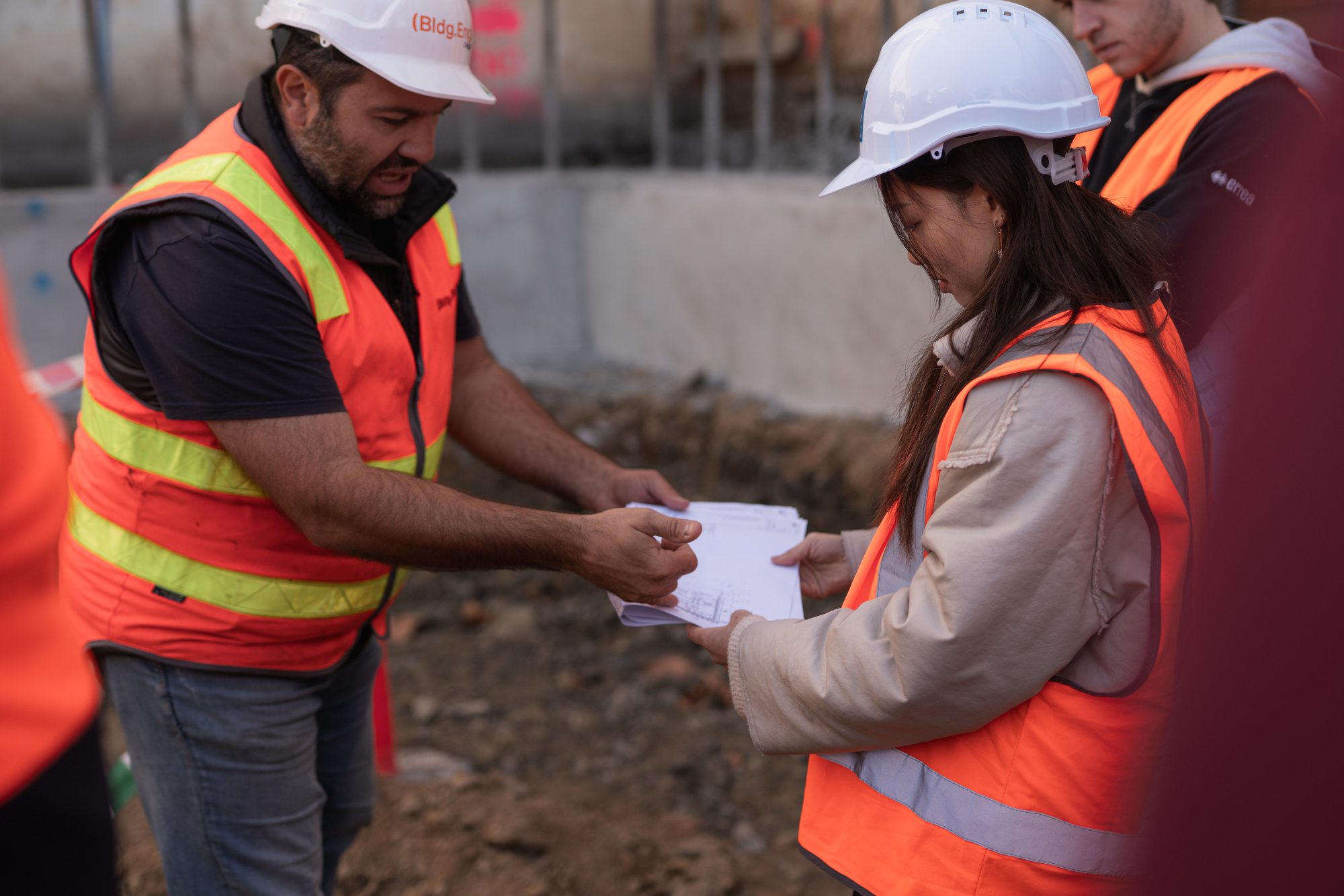 A construction site worker in PPE shows a plan to a student