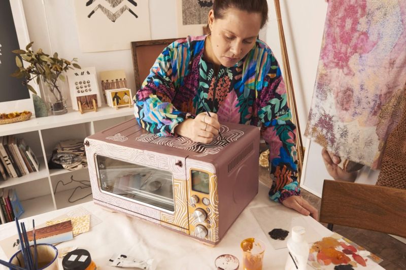 A woman stands in a studio painting an air fryer