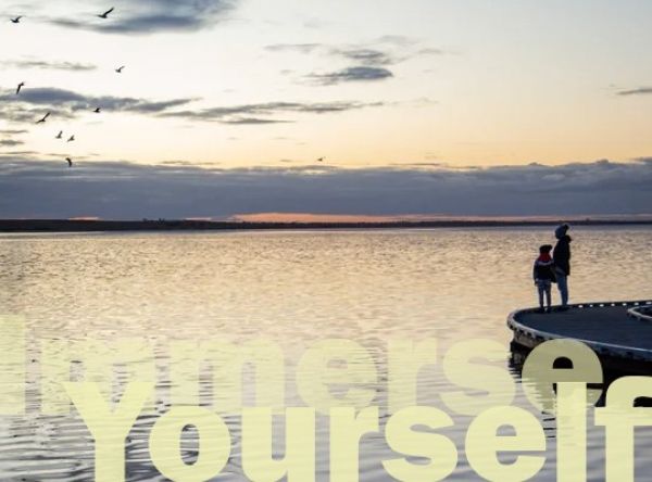 Two people look out over a lake from the shoreline