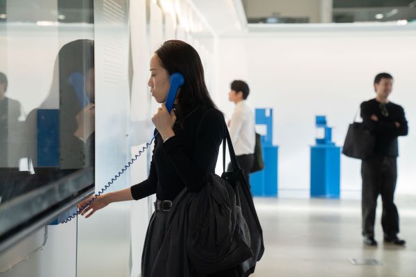Image of woman holding blue telephone to ear in exhibition.